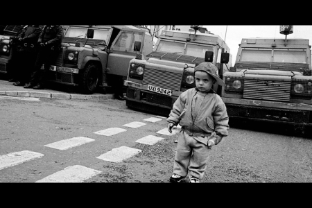 2. Black and white still of little boy in front of armoured police wagons